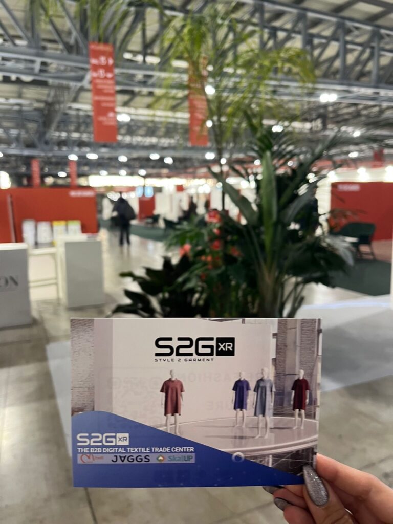 S2G XR flyer held at Milano Unica 2025 with the textile trade fair in the background, highlighting the digital B2B platform