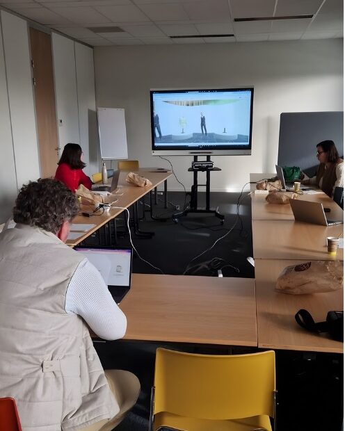 View of a plenary meeting at The Gate, showing partners watching a digital showroom demo on a large screen, seen from the back of the room.