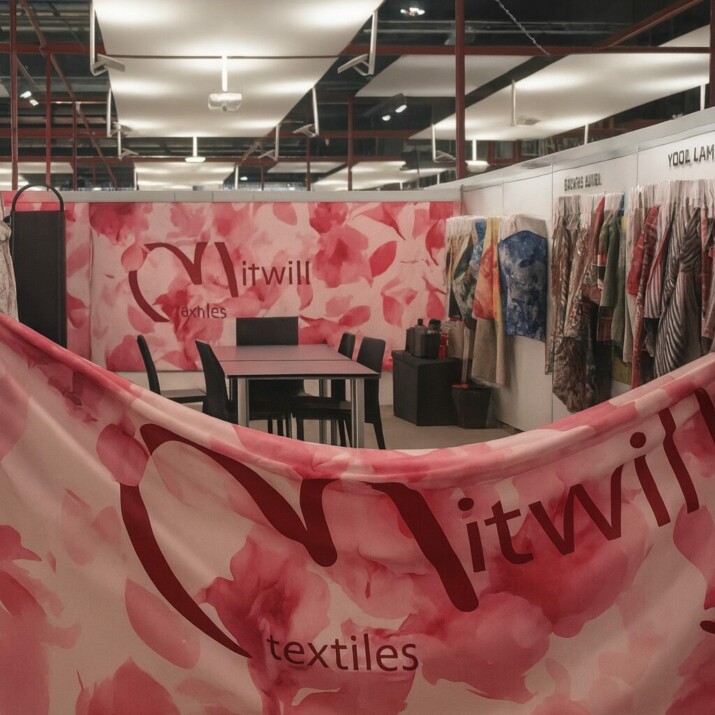 Mitwill Textiles booth at Milano Unica trade fair, with pink floral fabric and colorful samples displayed on the walls.